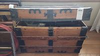 Front and side view of the antique wooden trunk showing metal reinforcements, rivets, and signs of wear.
