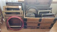 Multiple antique wooden frames stacked in a crate, including a distinctive large round red frame and several rectangular frames showing wear.
