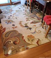 Full view of the multicolor area rug with floral and scroll patterns on a hardwood floor near furniture.