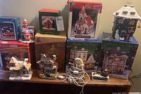 Full display of nine Christmas and Halloween themed porcelain light-up village houses and their original boxes.