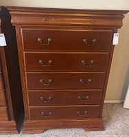 Front view of a tall wooden dresser with five large drawers and one smaller top drawer, showing warm brown finish and classic metal handles.