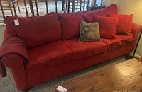 Front and angled view of large red microfiber couch showing rolled arms, cushions, and a decorative pillow.
