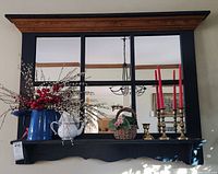 Front view of the mirror showing the shelf with decorative items including blue enamelware pitcher with faux berries, white pitcher, basket, and brass candlesticks with red candles.