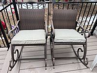 Front view of two brown metal rocking chairs with beige cushions on porch deck