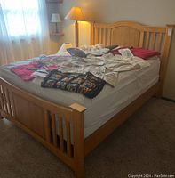 Full view of queen size bed frame with wooden slatted headboard and footboard, mattress and bedding on top.