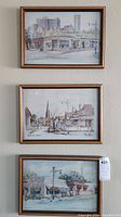 Three framed watercolor paintings hung on a wall, showing different street scenes. Two paintings are signed 'Mary Hulme.'