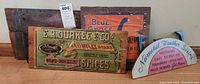 Vintage antique wood advertising signs stacked and arranged on floor and against wall, showing wear and paint aging.