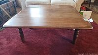 Front angle view of rectangular wooden coffee table with dropleaf unfolded, showing medium brown finish and turned legs.