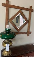 Full view of vintage brass oil lamp with green fleur-de-lis glass shade below wooden diamond frame mirror