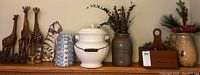 Wide shelf view showing all five lot items: chamber pot, blue and white pitcher, stamped crock, yellow pitcher, wooden tote