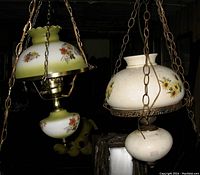 Two vintage Gone with the Wind hanging lamps with floral painted glass shades and chain hangers, displayed hanging from ceiling in a dim room.
