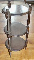 Photo of one walnut 3-tier round end table, showing the round wooden top, two tiers below, turned legs, and finial tops.