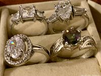 Close view of four ladies rings in a display box showing clear and iridescent crystal stones and silver-tone bands.