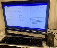 Front view of Acer Aspire Z3771 desktop computer showing BIOS screen with system info including Intel Pentium G630 CPU, 4GB RAM, and build date 08/26/2011. Keyboard and power adapter placed below monitor.