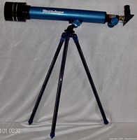 Full view of blue die-cast body telescope mounted on adjustable tripod stand, showing side view with brand name visible.
