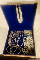 Wide view of open blue velvet-lined box showing multiple pearl necklaces, earrings, and loose beads.