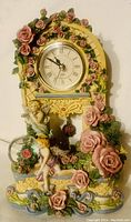 Front view of cherub angel floral table top clock showing clock face surrounded by roses and cherub figure sitting beside the clock.