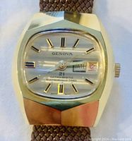 Front view of Genova men's gold toned watch with date screen, silver dial and brown woven strap.