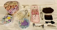 Photo shows assorted ladies accessories arranged on a flat surface including nail care kit, jewelry boxes, coin purses, eyelash curler, and other small items.