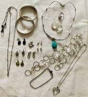 Assortment of ladies jewelry including bracelets, a ring, various earrings, and necklaces laid flat on a light surface.
