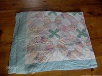 Full view of the quilt with folded edges showing flower and cross patch pattern and light blue border.