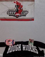 Photo showing Grey Cup banner, Rough Riders shirt, autographed football, and Jeff Pilon card arranged against a white wall.