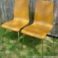 Photo showing the pair of mid-century modern teak finish chairs with chrome legs, from an angled side view outside.