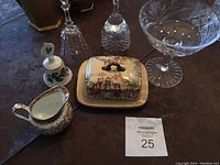 Photo showing a collection of items: crystal bell, English ceramic butter dish with lid, creamer with floral decoration, crystal candy dish, and other glass items on a table.
