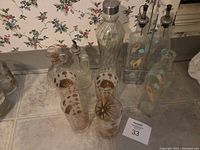 Full lot overview showing oil dispensers, dressing dispensers, and decorated drinking glasses on countertop with floral wallpaper background.