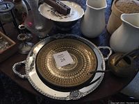 Overview photo showing multiple items on a wooden table including silver trays, ceramic pitchers, glass vases, woven basket, and figurines