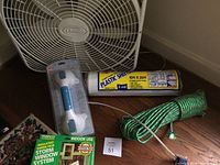 Lasso electric box fan, green rope, roll of plastic sheeting, and new grip handle in packaging on floor
