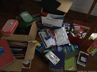 Photo showing a variety of office supplies scattered on the floor including boxes with portfolios, staplers, rulers, pencil boxes, Scotch tape rolls, and mechanical pencils.