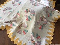 Shows full view of one large yellow quilt with pastel multi-colored circle fan blocks on white background and yellow scalloped edges