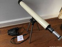 Photo showing the small tabletop telescope on a folded metal tripod beside the Nikon Eagleview binoculars on a wooden floor.