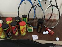 Full view of racquets and unopened tennis ball cans on floor showing brands and condition