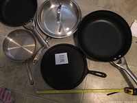Five skillets arranged on floor showing variety including vintage cast iron, Calphalon Teflon and aluminum skillets and stainless steel skillet.