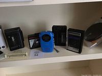 Five portable vintage audio devices on shelf including Sony Walkmans and a blue Brookstone radio
