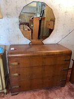 Full view of the wood waterfall style dresser with three drawers and attached octagonal mirror on top.