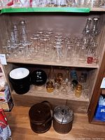 Shelf and floor showing multiple glassware items including stemware, small bottles, Bowler's decanter, and two ice buckets.
