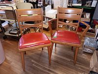 Pair of wooden armless chairs with red vinyl padded seats, showing two chairs side-by-side on hardwood floor
