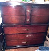 Full front view of dark wooden dresser showing four drawers with decorative brass handles.