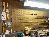 Five fishing rods with reels hanging horizontally on pegboard.