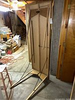 Wood folding table standing upright, showing underside and leg support with metal braces.