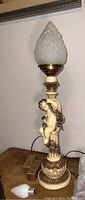 View of full lamp showing cherub figure and pinecone glass shade on top, with extra bulbs placed nearby on table.