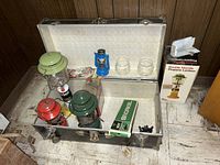 Metal trunk open showing three kerosene lanterns (green, red, blue), a green propane lantern on yellow base, new snorkel box, two glass jars, and small accessories inside.