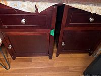 Pair of dark wood nightstands side by side, showing fronts with drawer and cabinet door, with visible scratches and wear
