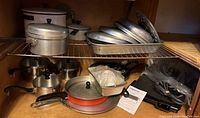 Shelf with various pots and pans including enamel saucepans, glass lids, and metal pans.