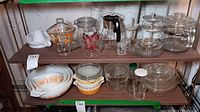 Overall view of two shelves displaying mixing bowls, casserole dishes, percolator, and various glassware