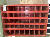Front view of red metal storage cubby with multiple square compartments, showing rust and chipped paint