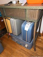 Front view of green wicker table showing woven wicker drawer, worn wooden top, standing on four legs with items beneath.